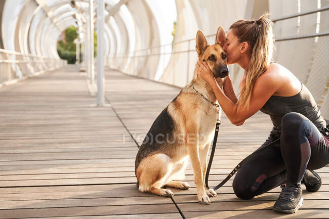 Woman in sportswear kissing German Shepherd dog on leash during running workout in daytime — Stock Photo