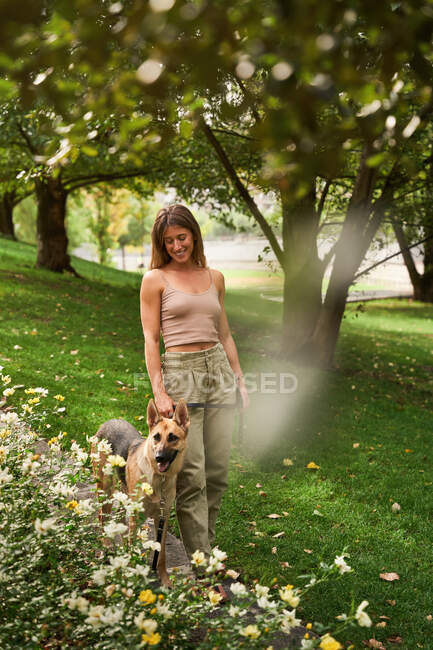 Corpo inteiro de proprietário feminino positivo andando cão pastor alemão no parque — Fotografia de Stock