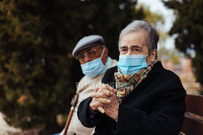 Vue latérale d'un couple âgé portant un masque facial dans la rue alors qu'ils regardent la caméra un après-midi d'hiver — Photo de stock