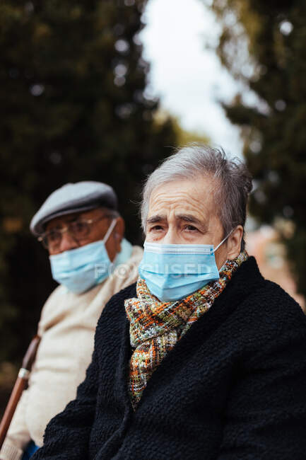 Vista lateral de una pareja de ancianos con mascarilla en la calle mientras miran a la cámara en una tarde de invierno - foto de stock