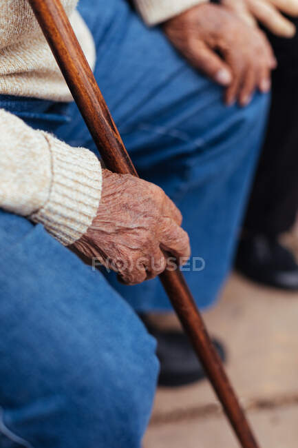 Pessoa idosa anônima segurando cana enquanto sentado no banco do parque — Fotografia de Stock