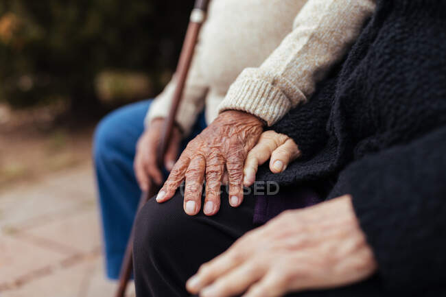 Recadrage de couples âgés anonymes tenant la main assis sur un banc de parc — Photo de stock