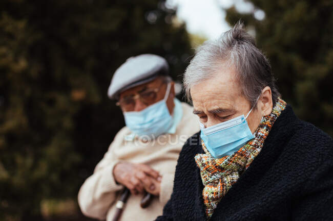 Vista lateral de una pareja de ancianos que usan mascarilla en la calle mientras miran hacia otro lado en una tarde de invierno - foto de stock
