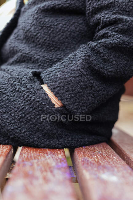 Side view of an anonymous elderly woman reaching into her coat pocket while sitting on a wooden park bench — Stock Photo