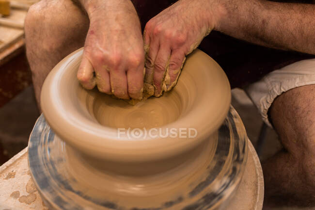 Cultivo escultor irreconocible con equipo que da forma mientras esculpe con arcilla marrón en la rueda de lanzamiento - foto de stock