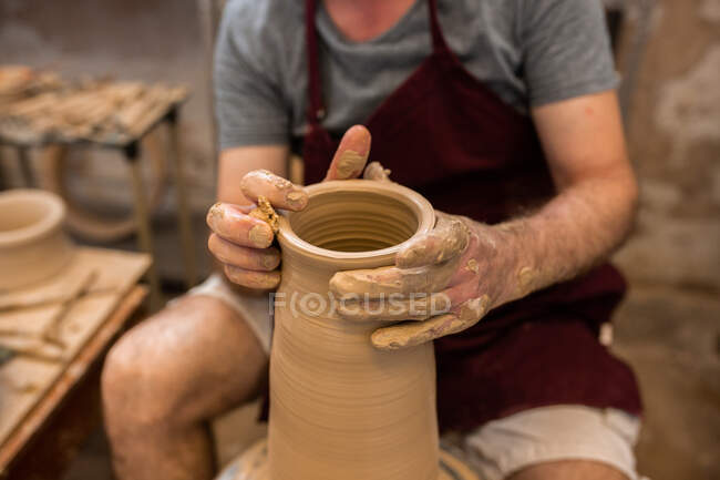 Crop unrecognizable sculptor with equipment giving shape while sculpting with brown clay on throwing wheel — Stock Photo