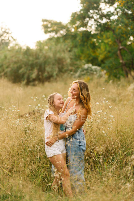 Vue latérale de sœur aimante embrassant tendrement adolescente debout dans la prairie en été — Photo de stock