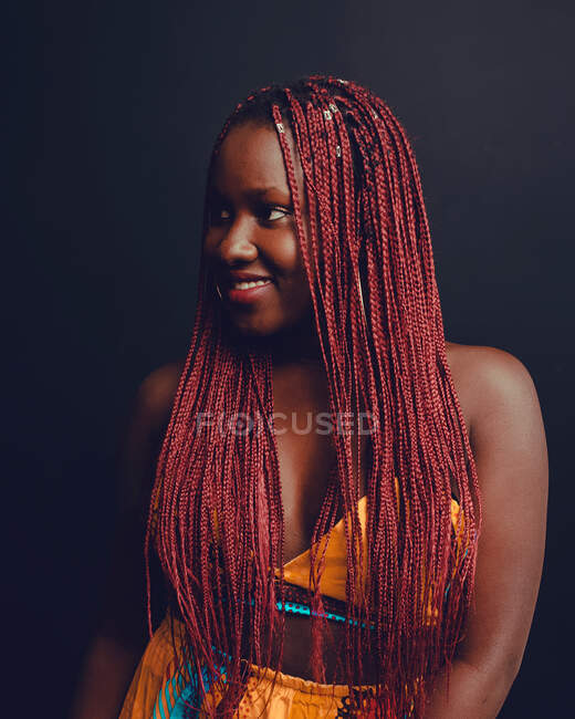 Cheerful African American female with pink braids standing on black background in studio and looking away — Stock Photo