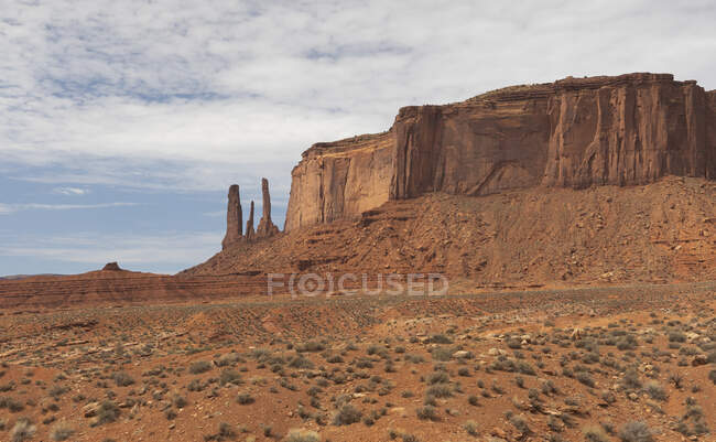Amazing landscape with rocky formations and poles located on dry terrain with shrubs  against cloudy sky in national park of USA — Stock Photo
