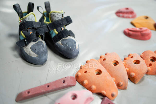 Various climbing holds and professional shoes for albinism on mat in bouldering center — Stock Photo