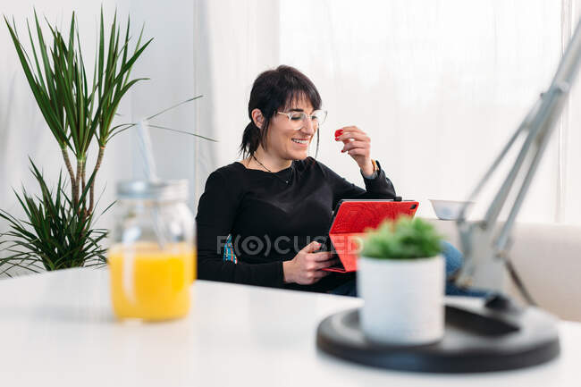 Glad female sitting on sofa and watching funny movie on tablet while relaxing at weekend at home — Stock Photo