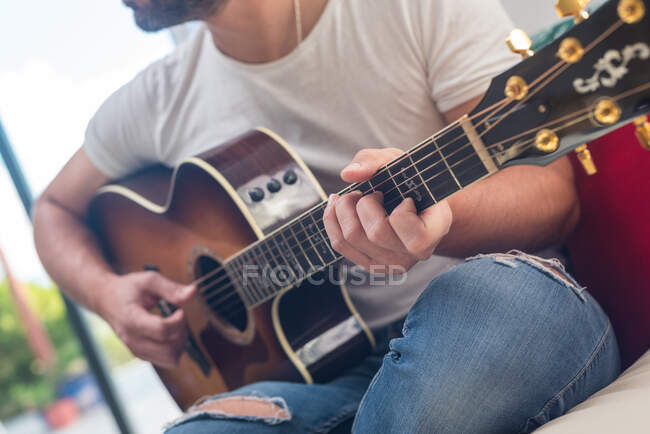 Урожай неузнаваемого бородатого музыканта, играющего на акустической гитаре на диване — стоковое фото