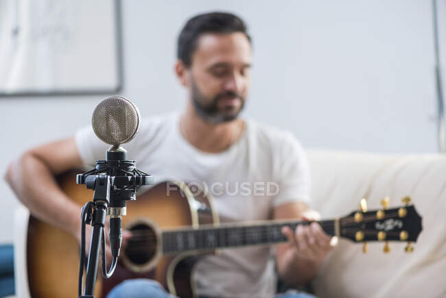 Vintage microphone near crop unrecognizable bearded male musician playing acoustic guitar on sofa — Stock Photo