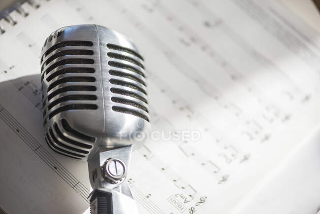 De cima de metal microfone vintage colocado em notas de música durante o ensaio à luz do dia — Fotografia de Stock