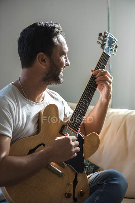 Erwachsene ethnische männliche Musiker in lässiger Kleidung relaxen auf bequemen Sofas und spielen zu Hause Akustikgitarre — Stockfoto