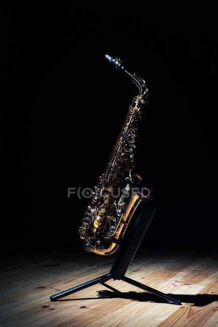 Saxophone ténor doré brillant sur pied placé sur scène en bois sur fond noir — Photo de stock