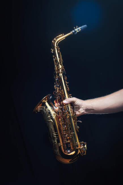 Анонимный музыкант демонстрирует золотой блестящий альт-саксофон, стоя на сцене на тёмном фоне. — стоковое фото