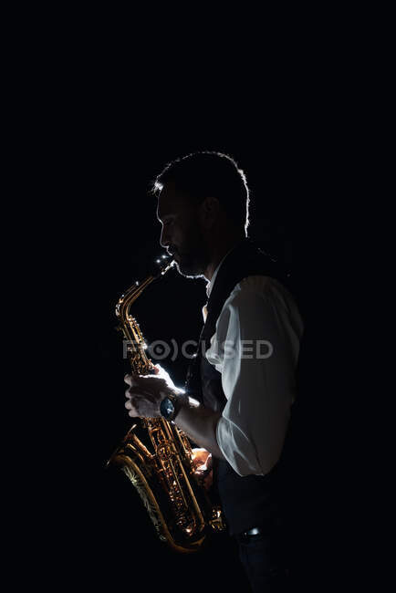Вид сбоку на музыканта в стильном костюме, играющего на альт-саксофоне во время джазового концерта — стоковое фото