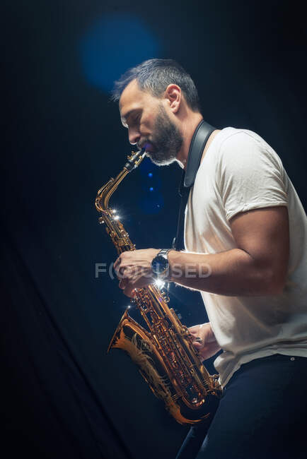 Vista lateral do músico masculino em roupa elegante tocando saxofone alto durante o concerto de jazz — Fotografia de Stock