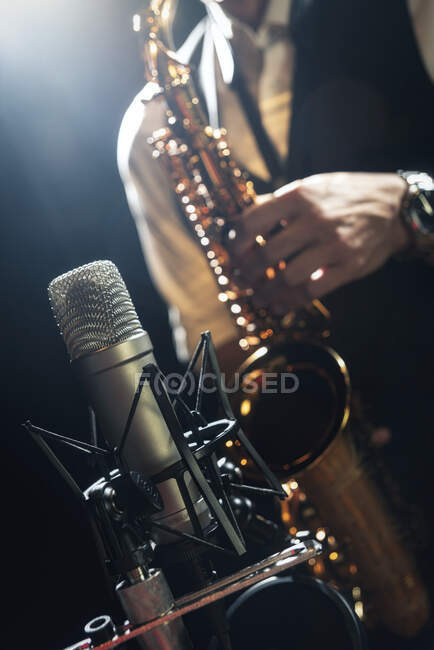 Crop unrecognizable male musician in classy outfit standing near microphone and playing alto saxophone during jazz concert — Stock Photo
