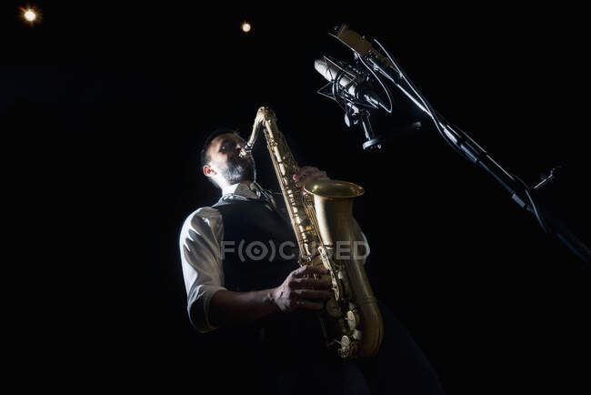 From below crop of male musician in classy outfit standing near microphone and playing alto saxophone during jazz concert — Stock Photo