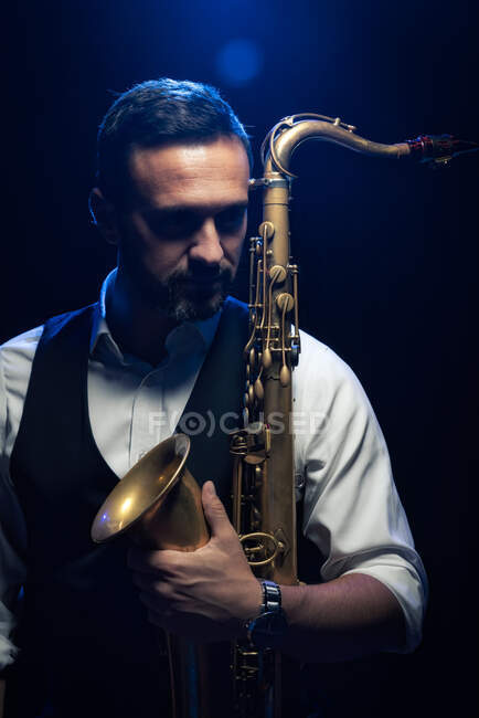 Портрет бородатого музыканта в элегантном наряде с саксофоном, стоящего на сцене во время концерта — стоковое фото