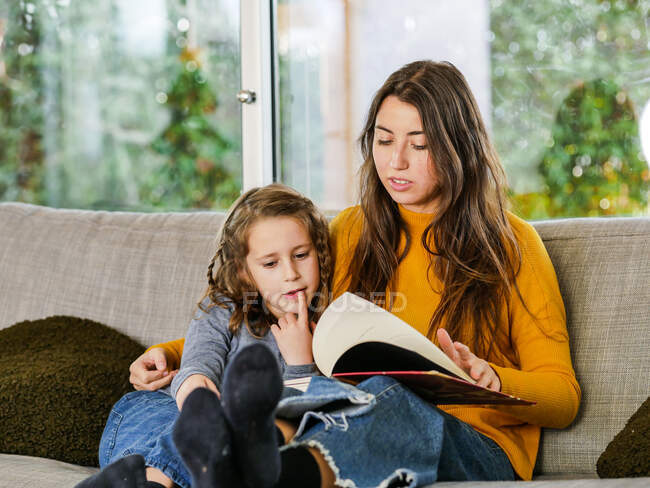 Содержание девушки подросток глядя на страницу учебника, в то время как проводить время с братом на диване дома — стоковое фото