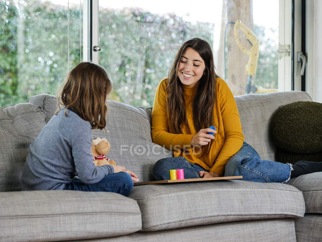 Conteúdo adolescente com irmã irreconhecível jogando jogo no sofá macio enquanto passa o tempo em casa — Fotografia de Stock