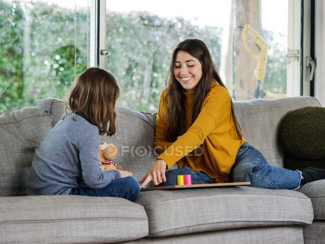 Contenu adolescent féminin avec soeur méconnaissable jouer au jeu sur un canapé doux tout en passant du temps dans la maison — Photo de stock