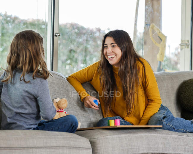 Conteúdo adolescente com irmã irreconhecível jogando jogo no sofá macio enquanto passa o tempo em casa — Fotografia de Stock