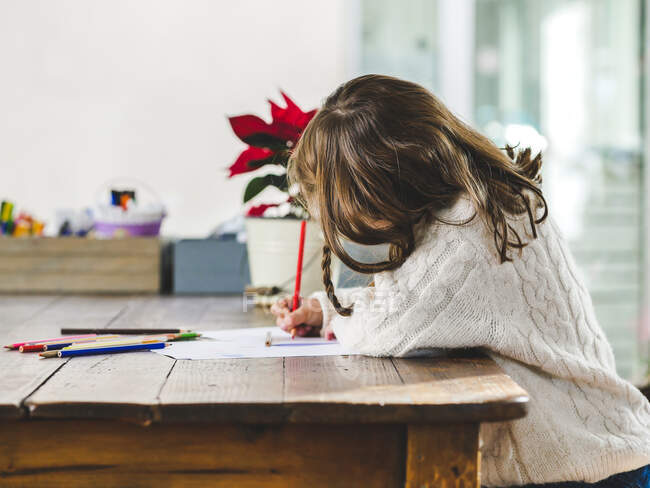 Анонимные рисунки маленькой девочки с разноцветными карандашами на бумажном листе в светлой комнате — стоковое фото