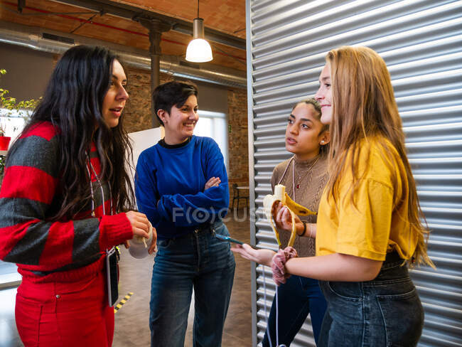 Young female classmates in casual wear standing close while talking about studying in corridor of university — Stock Photo