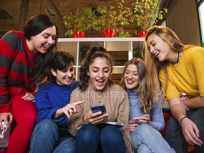 Estudiantes sonrientes sentadas en un sofá con smartphone y divirtiéndose durante el descanso - foto de stock