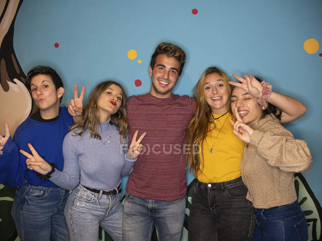 Jovens mulheres felizes e homem sorrindo brilhantemente enquanto estão juntos contra a parede pintada colorida e olhando para a câmera — Fotografia de Stock