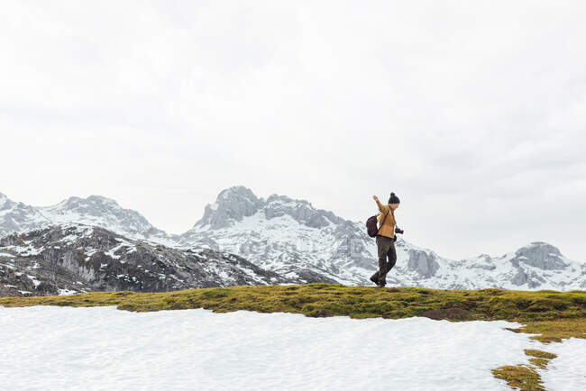 Весела жінка в теплому одязі, що піднімає руки в збудженні, стоячи на величезній гірській долині, вкритій снігом і оточені скелястими важкими горами — стокове фото