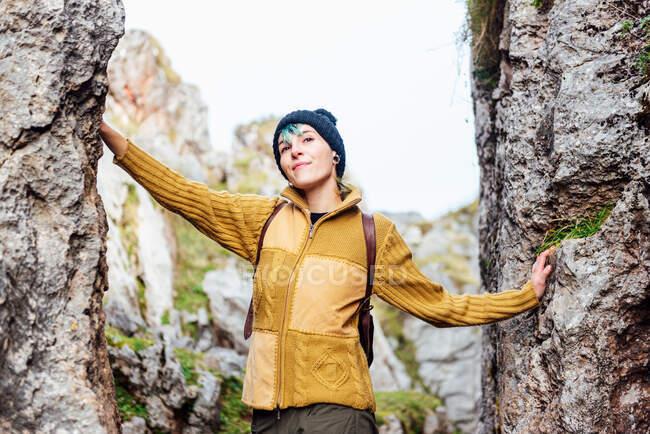Positive young woman in casual wear and hat standing amidst rocky formations and looking away contentedly — Stock Photo