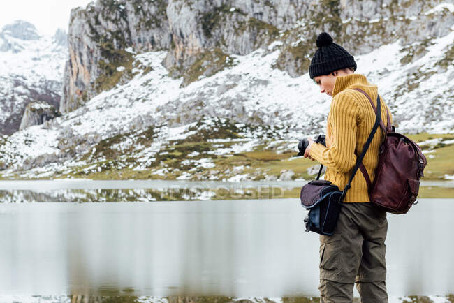 Вид збоку зосередив молоду жінку-фотографа в теплому светрі, фотографувавши професійну фотокамеру величних грубих гір на трав'янистих високогір'ях в чистий осінній день — стокове фото
