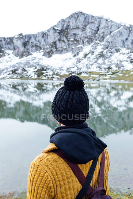 Back view of anonymous female with black hat standing on snowy rough highlands on lake shore — Stock Photo
