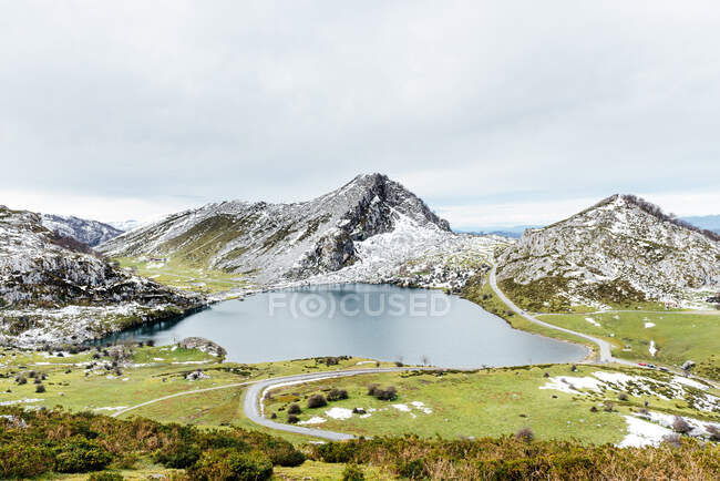 Spectacular view of rocky snowy mountain range near tranquil lake and spacious grassy valley in peaceful nature in Asturias — Stock Photo