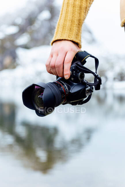 Crop anonymous female tourist in knitwear with professional photo camera against snowy mountain and lake in Asturias — Stock Photo