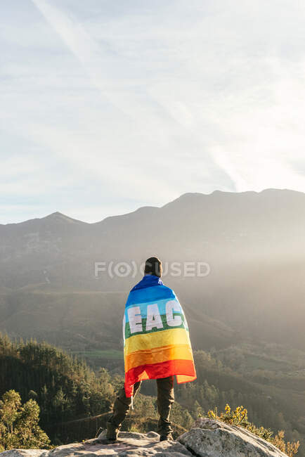 Rückansicht eines Wanderers, der mit einer Regenbogenfahne mit der Aufschrift Peace steht und die Freiheit in den Bergen genießt — Stockfoto