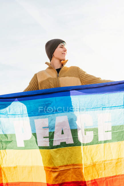 Caminante de pie con arco iris bandera LGBT con inscripción Paz y disfrutar de la libertad en las montañas - foto de stock