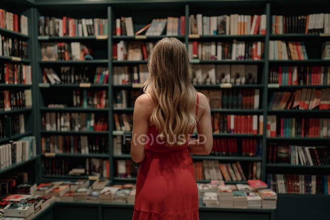 Vista posteriore di anonima donna elegante in prendisole in piedi contro tavolo con libri di testo assortiti in libreria — Foto stock