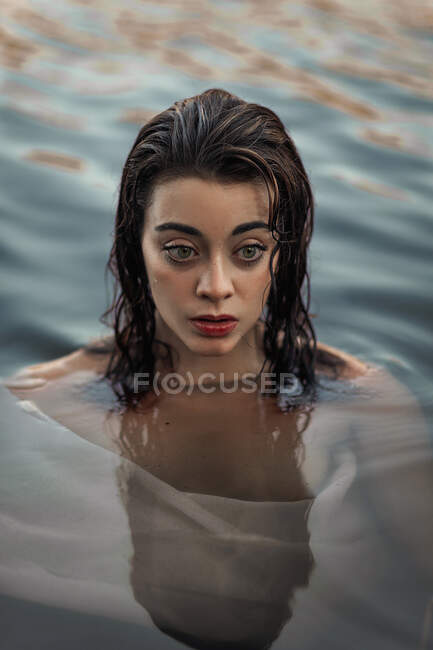 D'en haut de jeune voyageur féminin méditant avec le maquillage regardant loin dans l'eau pure ondulée — Photo de stock