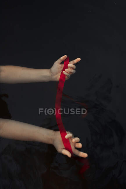 Top view of crop anonymous female traveler with reached arms demonstrating red blindfold in water on black background — Stock Photo