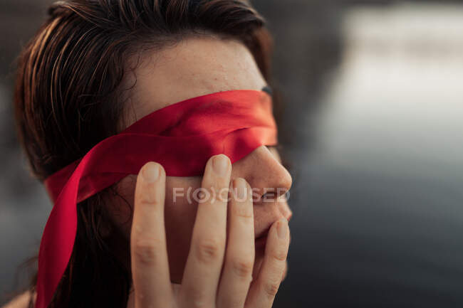 Vista lateral do turista fêmea gentil anônimo na venda vermelha tocando o rosto contra a água à luz do dia — Fotografia de Stock