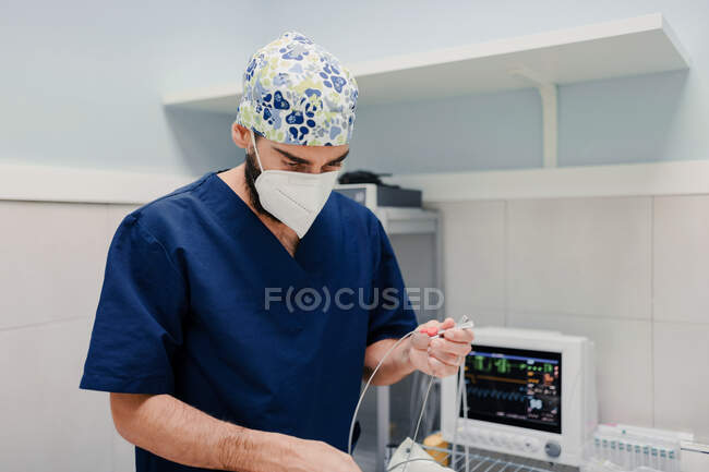 Chirurgien vétérinaire masculin méconnaissable en uniforme debout avec des câbles du moniteur ECG près de la table avec chat avant l'opération à l'hôpital — Photo de stock