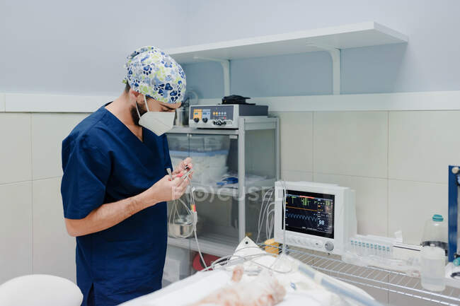 Unbekannter Tierarzt in Uniform steht mit Kabeln vom EKG-Monitor am Tisch mit Katze vor Operation im Krankenhaus — Stockfoto