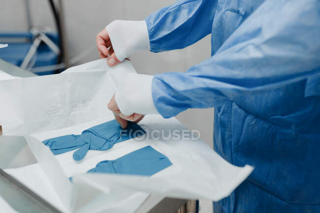 Crop view of anonymous young male veterinarian in sterile uniform putting on elastic gloves while preparing for surgery in operating room — Stock Photo