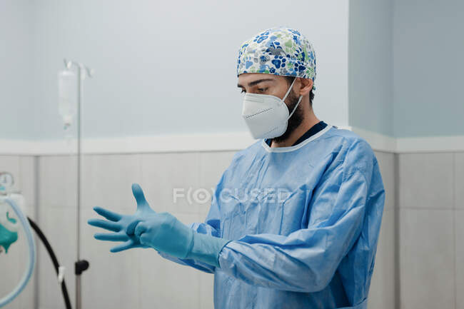 Anonyme jeune vétérinaire masculin en uniforme stérile portant des gants élastiques lors de la préparation à l'intervention chirurgicale en salle d'opération — Photo de stock